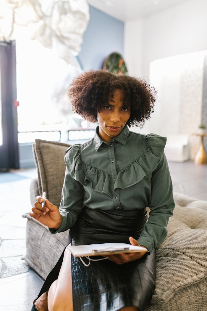 African American businesswoman with afro hair sitting on sofa holding clipboard in modern office.