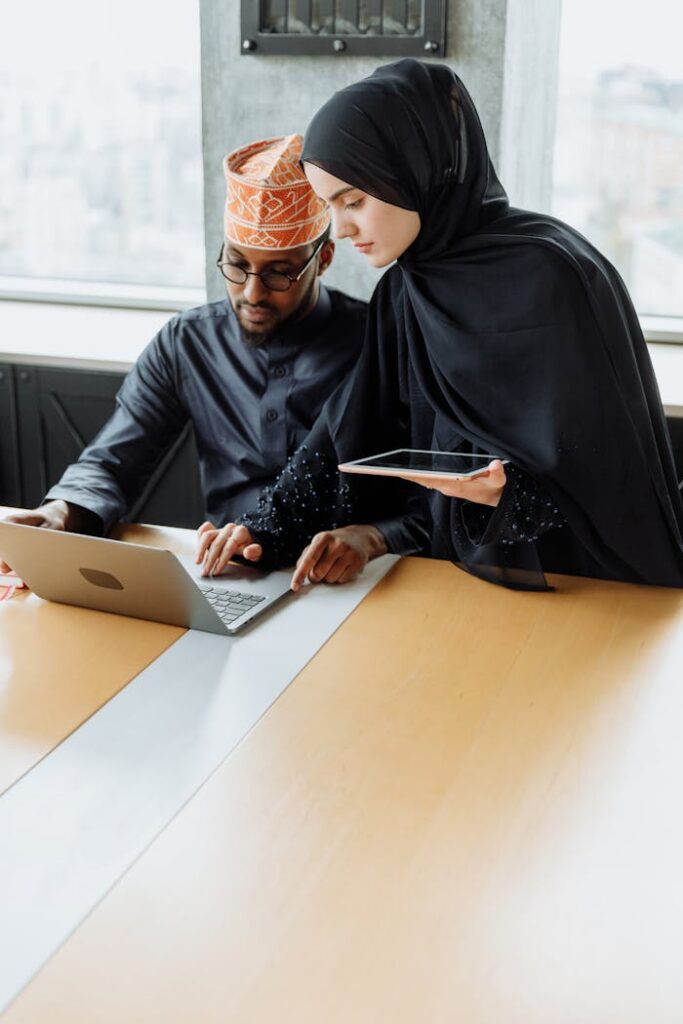 Man and woman in traditional attire working together on a laptop in an office.