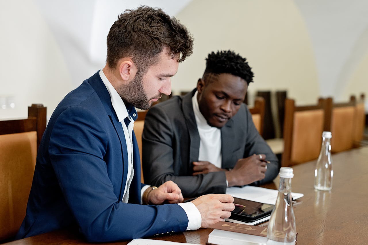 team-04 Two businessmen in suits discussing a project using a digital tablet during a business meeting indoors.